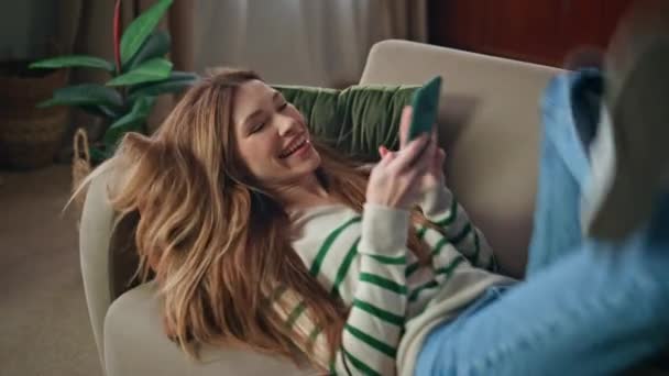 Šťastná dívka padající gauč dělat smartphone selfie detailní. Uvolněná krásná žena pomocí mobilní kamery na focení obličeje na útulné pohovce. Usmívání bezstarostný blogger relaxaci v bytě obývací pokoj - Záběry, video