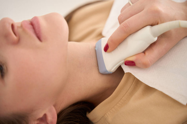 Закрыть обрезанное изображение женщины-врача, делающей ультразвуковое сканирование щитовидной железы молодой женщины в клинике. Концепция здравоохранения - Фото, изображение