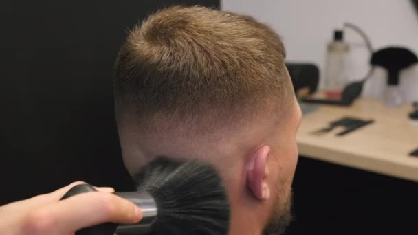 Fryzjer zamiata ścięte włosy z męskiego klienta kark pędzlem w fryzjera zbliżenie. Fryzjer dba o komfort człowieka podczas fryzury w salonie - Materiał filmowy, wideo