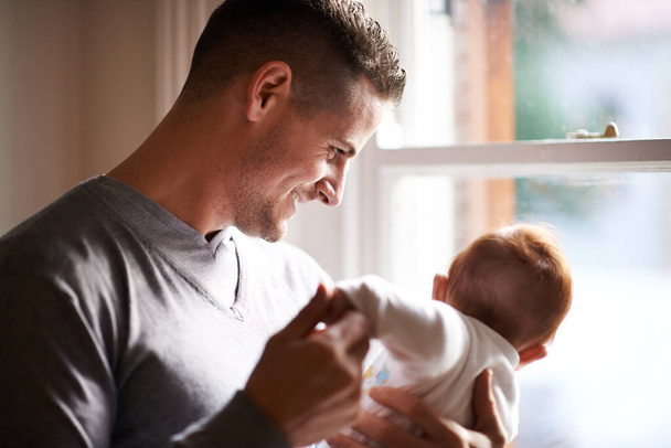 Father, baby and home with bonding, care and support together with family love at a window. Dad, smile and young child in a house with parent with newborn and man happy and proud about infant. - Photo, Image