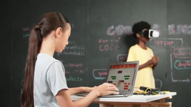 Afrikaanse jongen draagt VR terwijl Kaukasisch meisje laptop en draai je om om te zwaaien hand op camera. Volwassene staat aan blackboard met code en prompt geschreven terwijl vrouw begroet op camera. Edificatie - Video