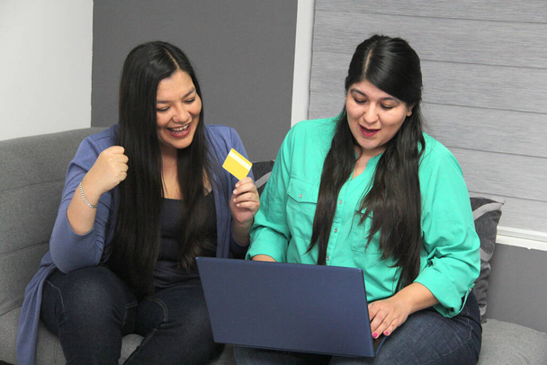 Дві дружні латиноамериканки використовують свій ноутбук і кредитну картку, щоб зробити покупки в Інтернеті здивовані знижками та акціями - Фото, зображення