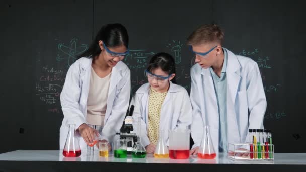 Menina inteligente derramar solução colorida para copo enquanto estudante diverso animado sobre fazer experimento. Cientista profissional se prepara para fazer experimentos em quadro-negro com teoria química. Edificação - Filmagem, Vídeo