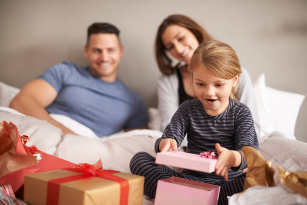 Ouders, kind en glimlach in de slaapkamer met cadeautje, verrassing en wow in huis voor de verjaardag. Moeder, vader en meisje met geluk en doos met lint voor ontvangst, gezin en waardering. - Foto, afbeelding