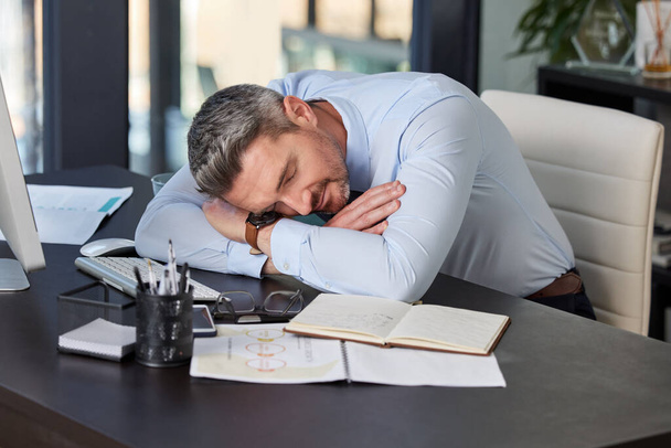 Fatigué, homme d'affaires et dormant au bureau avec repos, sieste ou épuisement professionnel. Employé épuisé, professionnel et masculin pour fatigue, stress lié à la date limite ou sommeil sur le lieu de travail. - Photo, image