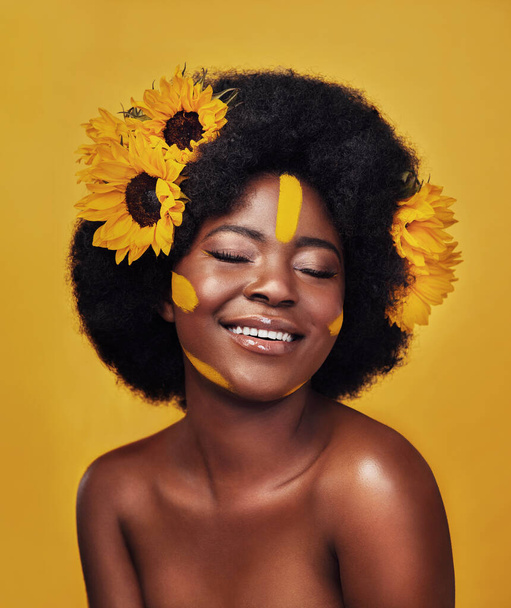 Μαύρη γυναίκα, χαρούμενη και ηλιοτρόπια με περιποίηση δέρματος στο στούντιο για δερματολογία, φυσική λάμψη ή βιταμίνη Ε. Άτομο, floral και μάτια κλειστά με χαμόγελο για οργανικό, καλλυντικό ή απαλό δέρμα σε κίτρινο φόντο. - Φωτογραφία, εικόνα