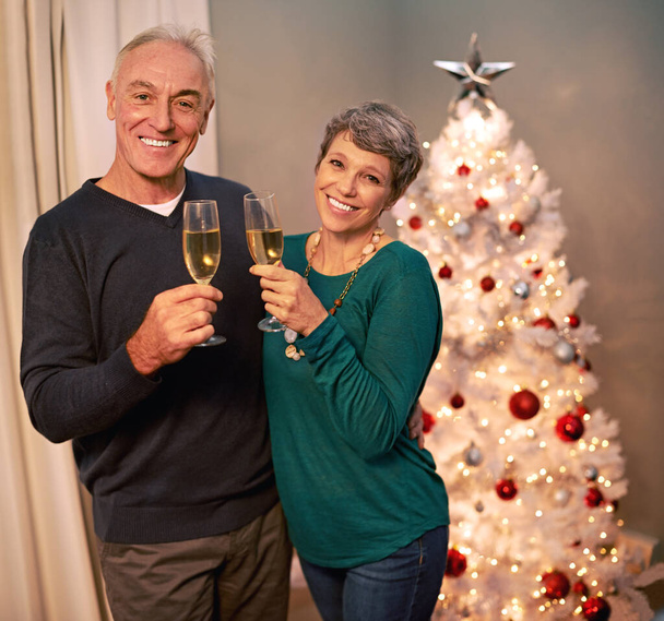 Christmas, portrait and champagne of senior couple with love, care and support in a home on holiday. Tree, retirement and marriage with a smile and hug in a house with celebration drink and cheers. - Photo, Image