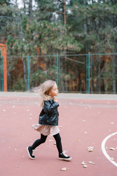 Kleines Mädchen mit fliegendem Haar läuft über den Sportplatz. Seitenansicht. Hochwertiges Foto - Foto, Bild