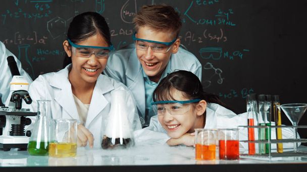 Dívka se dívá na kádinku při experimentu na tabuli s teorií chemie ve STEM třídě. učitel a skupina středoškolských studentů se smíšenými rasami, kteří spolu dělají vědeckou činnost. Edukační. - Fotografie, Obrázek