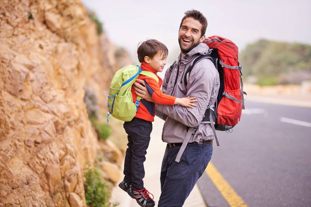 Father, child and portrait with hike, backpack and travel with smile and support in nature by road. Kid, adventure and laugh with love, trust and bonding together with family and journey for holiday. - Photo, Image