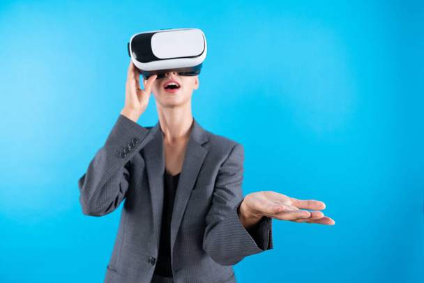 Üzletasszony VR szemüveggel áll és jelen ötlet magabiztosan áll a kék háttérben. Profi projektmenedzser öltönyt visel, miközben tart valamit. Technológia. Összekeverés. - Fotó, kép