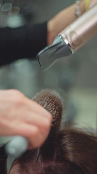 Een kapper doet styling voor een vrouw met behulp van een borstel en een haardroger. Een mooi meisje met schoonheidsbehandelingen in een kapsalon. Hoge kwaliteit 4k beeldmateriaal - Video