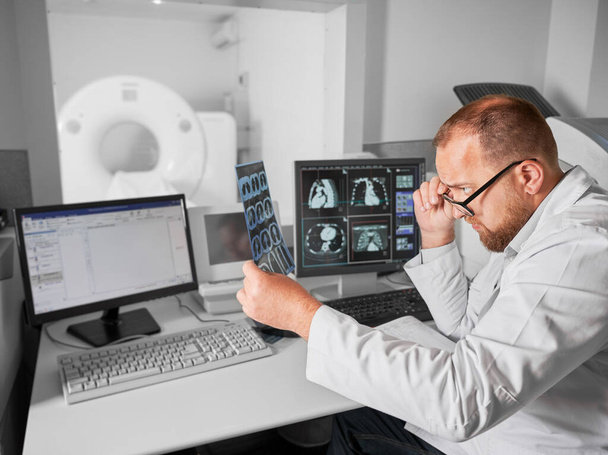 Orvosi komputertomográfia vagy MRI szkenner. Az MRI eredményeket vizsgáló férfi orvos oldalnézete. Szemüveget és fehér köpenyt viselő specialista, röntgent néz, tanul. Az orvostudomány és az egészségügy fogalma. - Fotó, kép