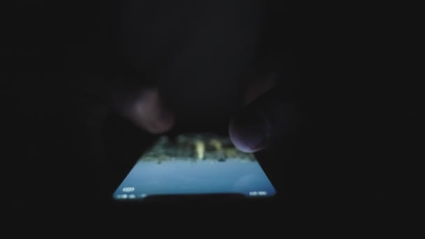 Mano masculina usando teléfono inteligente mientras se desliza en la pantalla por los dedos en la oscuridad. Tecnología, Internet, en línea, concepto de aplicaciones móviles. Movimiento lento - Imágenes, Vídeo