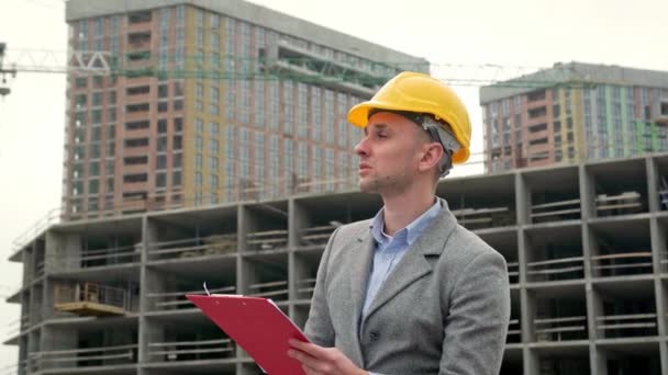 Портрет сфокусованого будівельного керівника, який консультує його кишеню, перевіряючи незавершені багатоповерхові будинки. Повільний рух - Кадри, відео