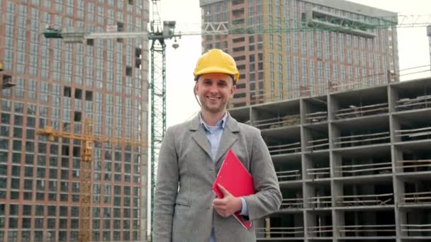 Радостный строительный аудитор с буфером под мышкой, стоящий среди недостроенных многоэтажных домов. Долли выстрелил - Кадры, видео