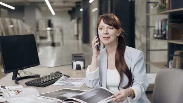 Женщина разговаривает по мобильному телефону на рабочем столе - Кадры, видео