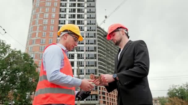 Építési menedzser ad készpénzt az építész, miközben kezet rázva előtt befejezetlen apartman épület. Lassú mozgás. - Felvétel, videó