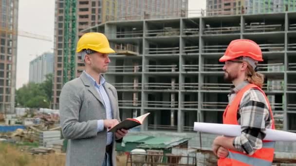 Ystävällinen rakennustarkastaja kättelee tyytyväistä työnjohtajaa kesken keskustelun keskeneräisen asuintalon edessä. Hidastus - Materiaali, video