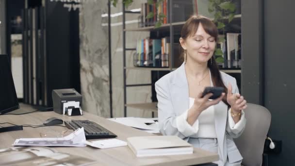 Female designer using cell phone at office desk - Footage, Video