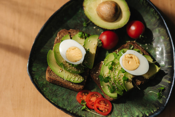 Evde sağlıklı bir kahvaltı. Avokado ve yumurtalı lezzetli sandviçler. Kirazlı domates ve mikroyeşil. Yüksek kalite fotoğraf - Fotoğraf, Görsel