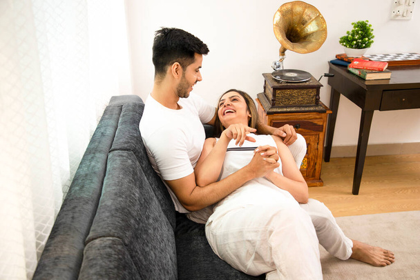 Smiling good couple in white outfit, woman lying on her husband lap in living room - Photo, Image