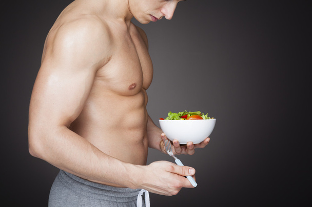 Fitness man holding a bowl of fresh salad - Фото, изображение