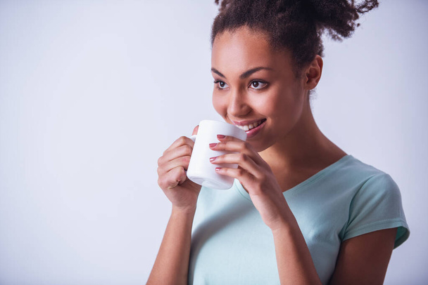 Веселая девушка в повседневной одежде держит чашку, смотрит в сторону и улыбается, изолирован на белом - Фото, изображение