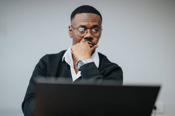 A contemplative African American businessman engaging deeply with statistical data on his computer in a modern office setting. - Photo, Image
