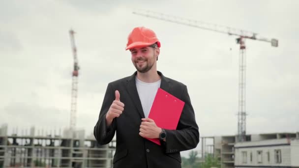 Construtor em terno de escritório e protetor capacete laranja segurando prancheta e mostrando classe sinal. Movimento lento - Filmagem, Vídeo