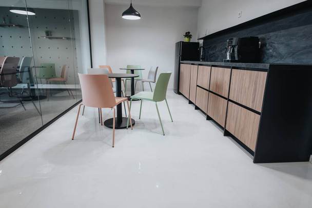 Moderne kantoor break kamer met levendige groene en perzik stoelen, een stijlvolle kitchenette en een glazen vergaderzaal. - Foto, afbeelding