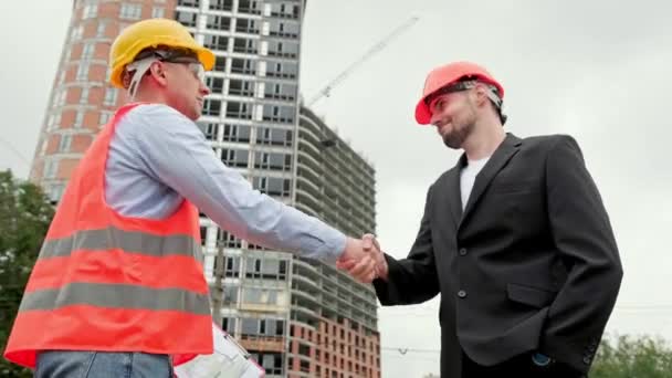 Foreman in vest, protective helmet and glasses standing near architect and shaking hands. Slow motion video - Footage, Video