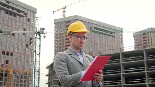 Foreman w kasku ochronnym stojący na miejscu, trzymający podkładkę i robiący notatki. Filmik o zwolnionym tempie - Materiał filmowy, wideo