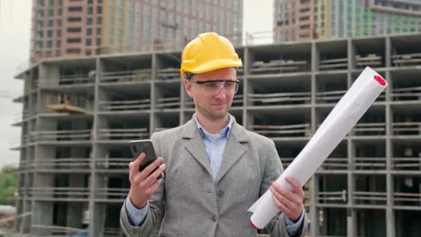 Foreman w kasku ochronnym stojący na miejscu, trzymający plan i pokazujący smartfona z zielonym ekranem. Filmik o zwolnionym tempie - Materiał filmowy, wideo