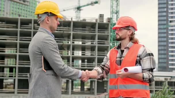 Foreman in vest, protective helmet and glasses standing near builder and shaking hands. Slow motion video - Footage, Video