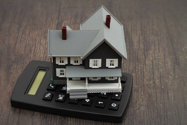 Een huis en rekenmachine op een houten bureau voor het berekenen van uw hypotheek met een onheilspellende stemming - Foto, afbeelding