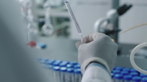Imágenes de cerca de las manos del técnico anónimo en guantes vertiendo líquido de la pipeta en el tubo de ensayo, mientras se realizan pruebas en el laboratorio de diagnóstico - Metraje, vídeo
