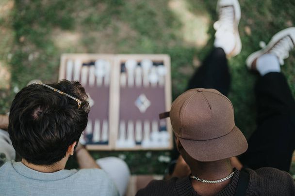 Zwei Freunde genießen an einem unbeschwerten sonnigen Tag ein Backgammon-Spiel im Freien. Lässig, lustig und fröhlich verkörpern sie Freude und Zusammengehörigkeit in einer Parkanlage. - Foto, Bild