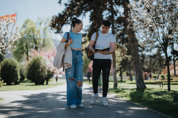 Két fiatal felnőtt tanul könyveket óra után egy nyüzsgő, napfényes városi parkban.. - Fotó, kép