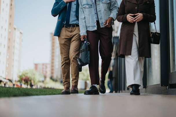 Profesjonaliści w stylowych strojach angażują się w rozmowę podczas spaceru ulicą miasta, niosąc torby i ubrani w strój służbowy casual. - Zdjęcie, obraz