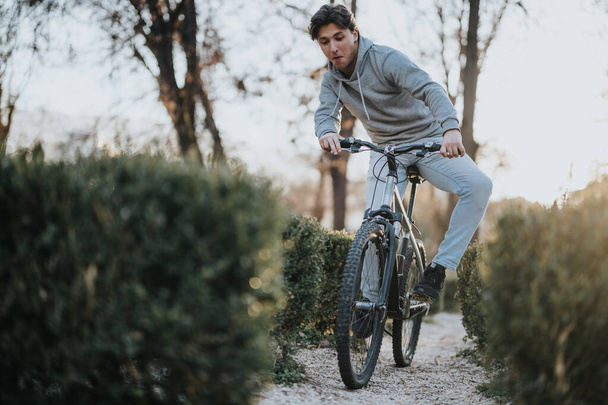 Keskittynyt mies pyöräilijä nauttimassa pyöräilystä puistopolkua pitkin, luonnon ympäröimänä auringonlaskun aikaan. - Valokuva, kuva