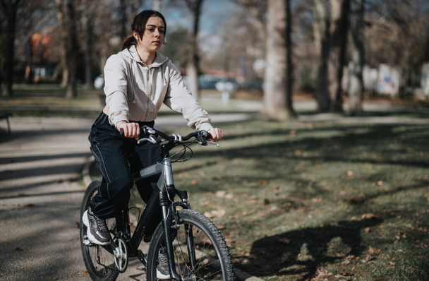 Egy derűs nap, amikor egy nő egy fákkal szegélyezett ösvényen biciklizik a parkban, egészséges életvitelt folytatva. - Fotó, kép