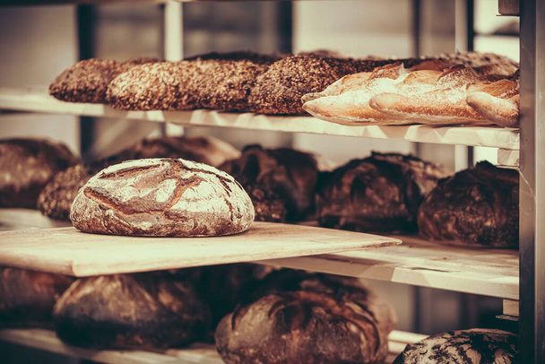 Frisch gebackenes Brot wird in einer Bäckerei in einen Holzregalwagen geschoben - Foto, Bild