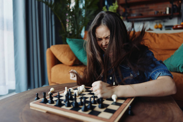 Vrouw geniet van een potje schaken op een houten plank in een gezellige woonkamer setting - Foto, afbeelding