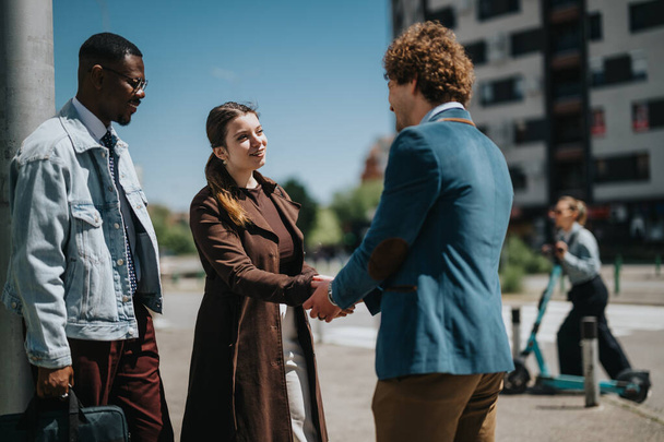A business meeting takes place outdoors where a woman and two men, all in professional attire, greet each other warmly in an urban setting. - Photo, Image