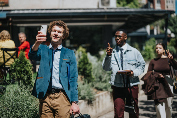 Jóvenes empresarios tomando selfie mientras están involucrados en un trabajo al aire libre, utilizando la tecnología, con la gente caminando en un entorno urbano ocupado. - Foto, imagen