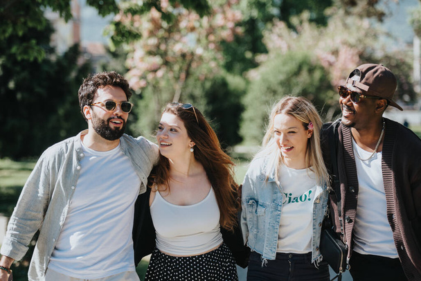 Négy többnemzetiségű barát osztozik az örömben és a nevetésben egy vidám séta során egy napfényes parkban, mely barátságot és boldogságot testesít meg.. - Fotó, kép
