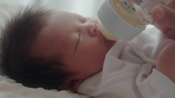 matka karmiąc córkę butelką mleka w domu - Materiał filmowy, wideo