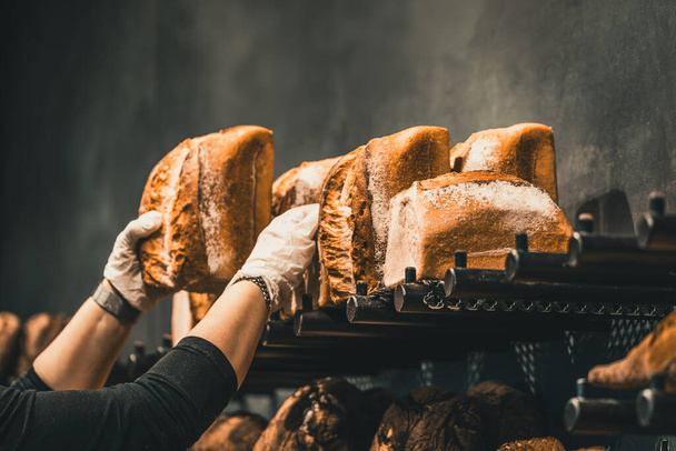 Hands of a saleswoman putting fresh bread on the shelf in the bakery, copy space - Photo, Image