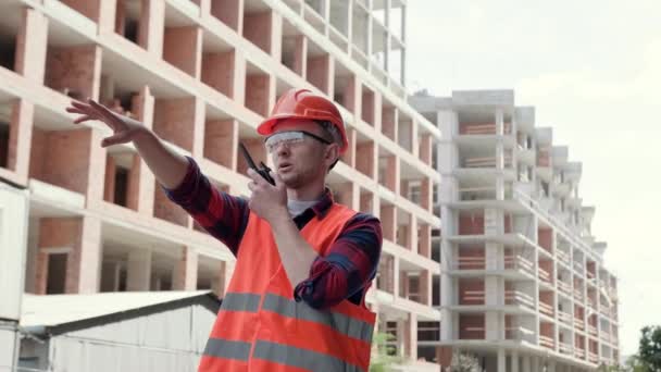 Stavební dělník komunikující obousměrným rádiem, zatímco stojí mezi nedokončenými vícepodlažními budovami. Zpomalený pohyb - Záběry, video